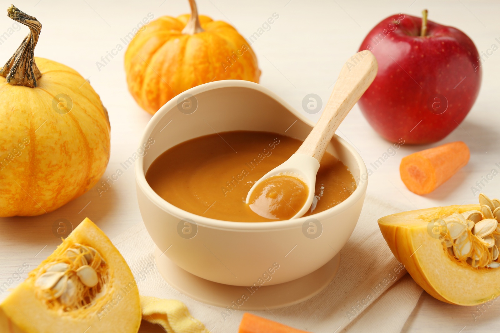 Photo of Delicious baby food with spoon in bowl and fresh ingredients on white wooden table