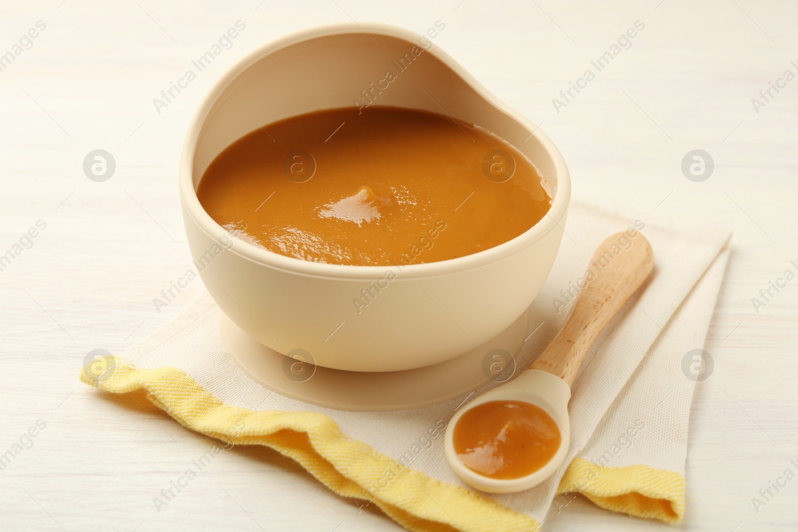 Photo of Delicious baby food in bowl and spoon on white wooden table