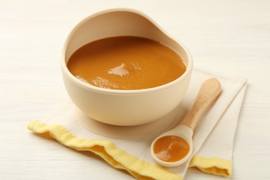 Photo of Delicious baby food in bowl and spoon on white wooden table