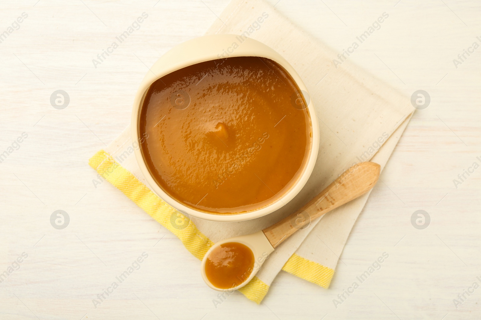 Photo of Delicious baby food in bowl and spoon on white wooden table, flat lay