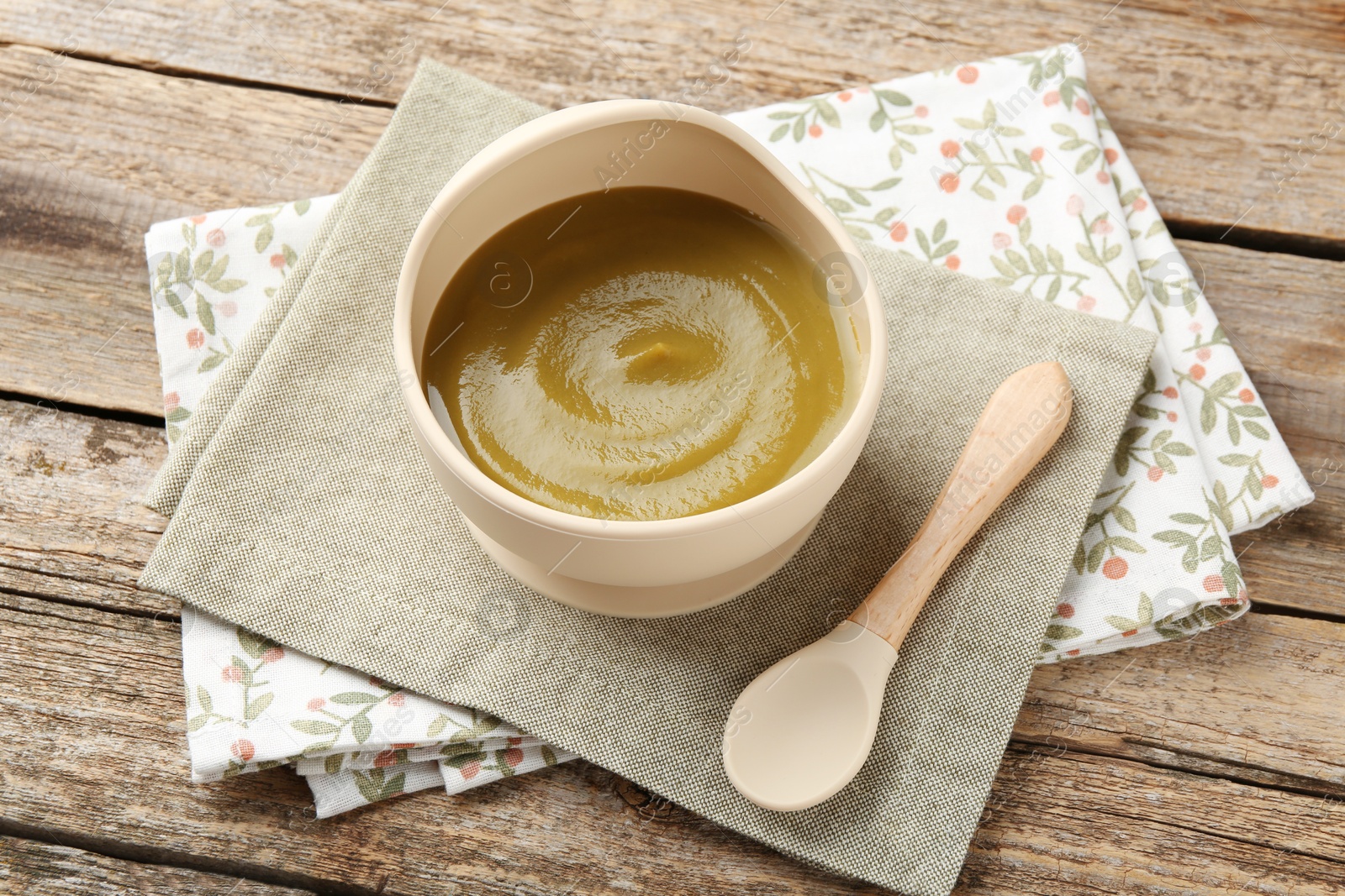 Photo of Delicious baby food in bowl with spoon on wooden table