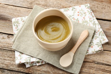 Photo of Delicious baby food in bowl with spoon on wooden table