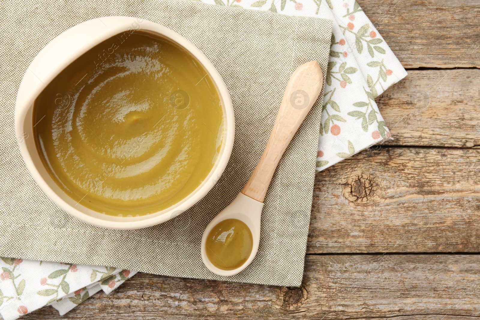 Photo of Delicious baby food in bowl with spoon on wooden table, flat lay