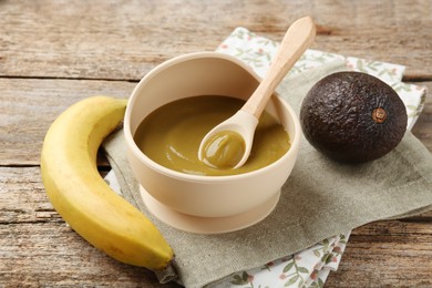 Photo of Delicious baby food with spoon in bowl and fresh ingredients on wooden table