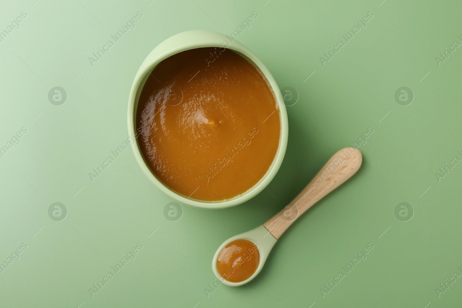 Photo of Delicious baby food in bowl with spoon on green table, flat lay