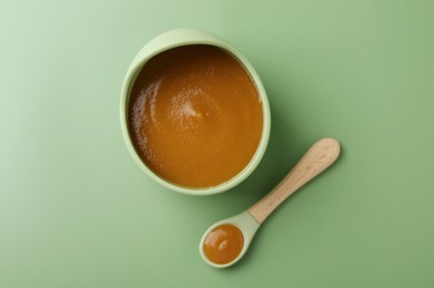 Photo of Delicious baby food in bowl with spoon on green table, flat lay