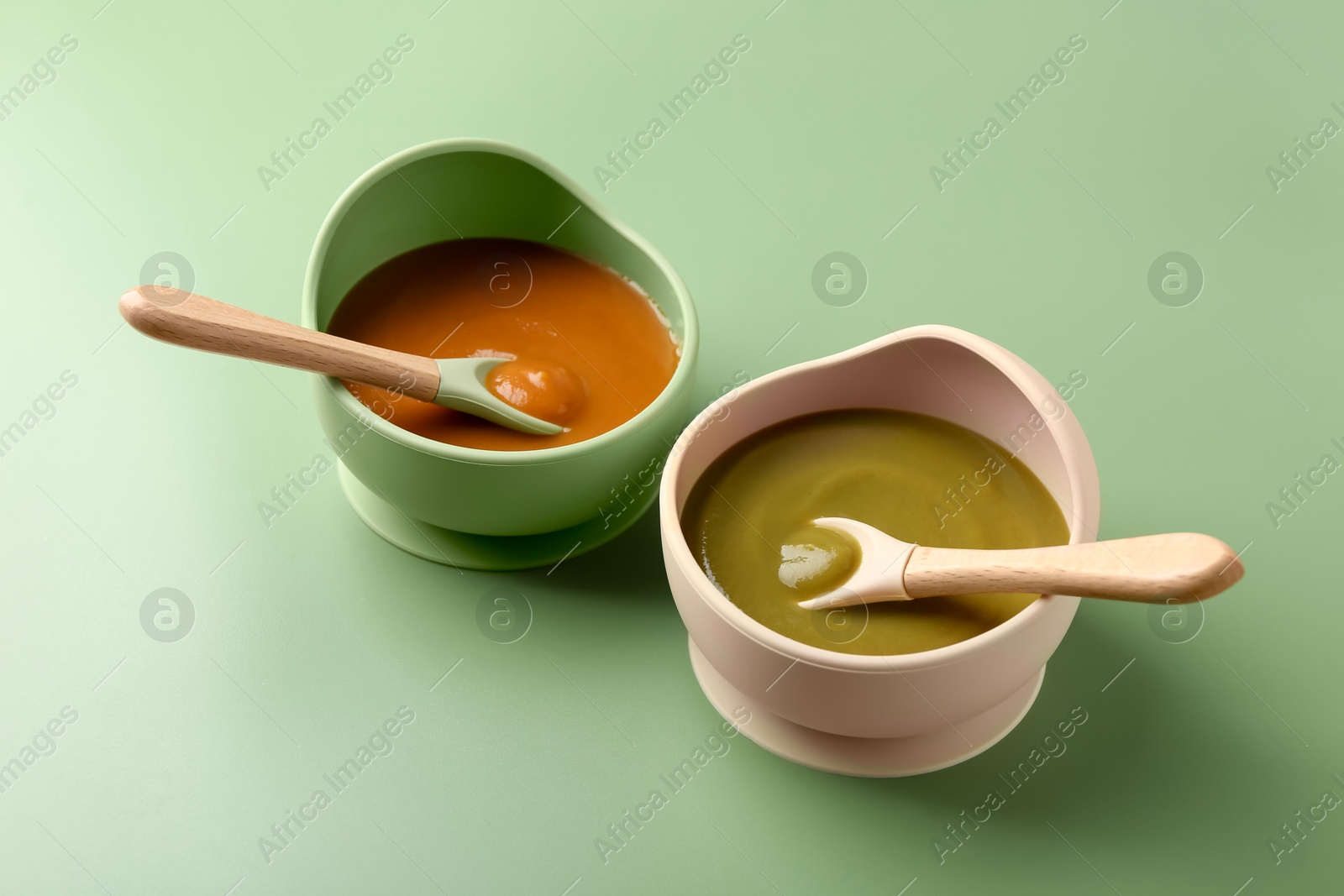 Photo of Delicious baby food with spoons in bowls on green table