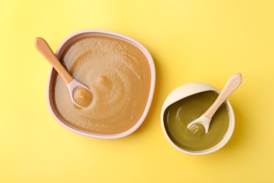 Photo of Delicious baby food and spoons in bowls on yellow table, flat lay