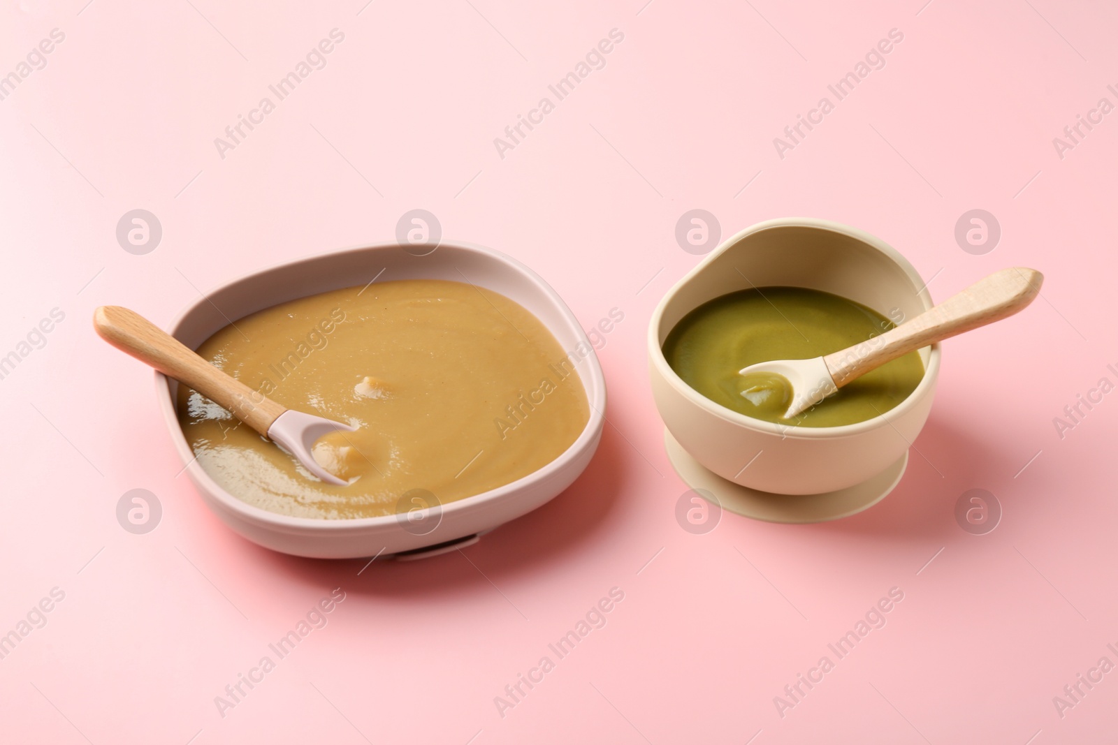 Photo of Delicious baby food and spoons in bowls on pink table