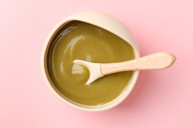 Photo of Delicious baby food with spoon in bowl on pink table, top view