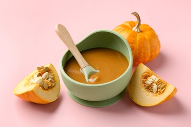 Photo of Delicious baby food with spoon in bowl and fresh pumpkins on pink table