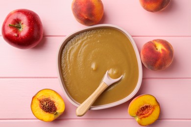 Photo of Delicious baby food with spoon in bowl and fresh ingredients on pink wooden table, flat lay