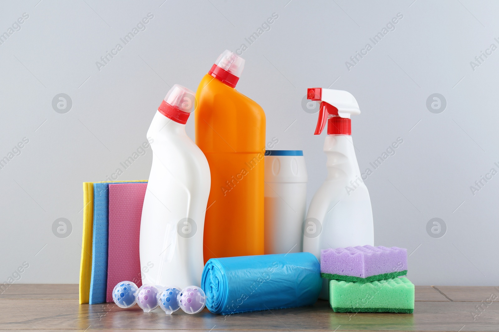 Photo of Different toilet cleaners, sponges and trash bags on wooden table against light grey background