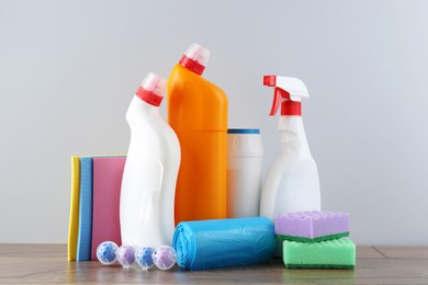 Photo of Different toilet cleaners, sponges and trash bags on wooden table against light grey background