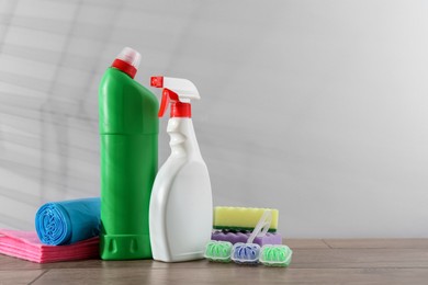 Photo of Different toilet cleaners, sponges and trash bags on wooden table against light grey background. Space for text