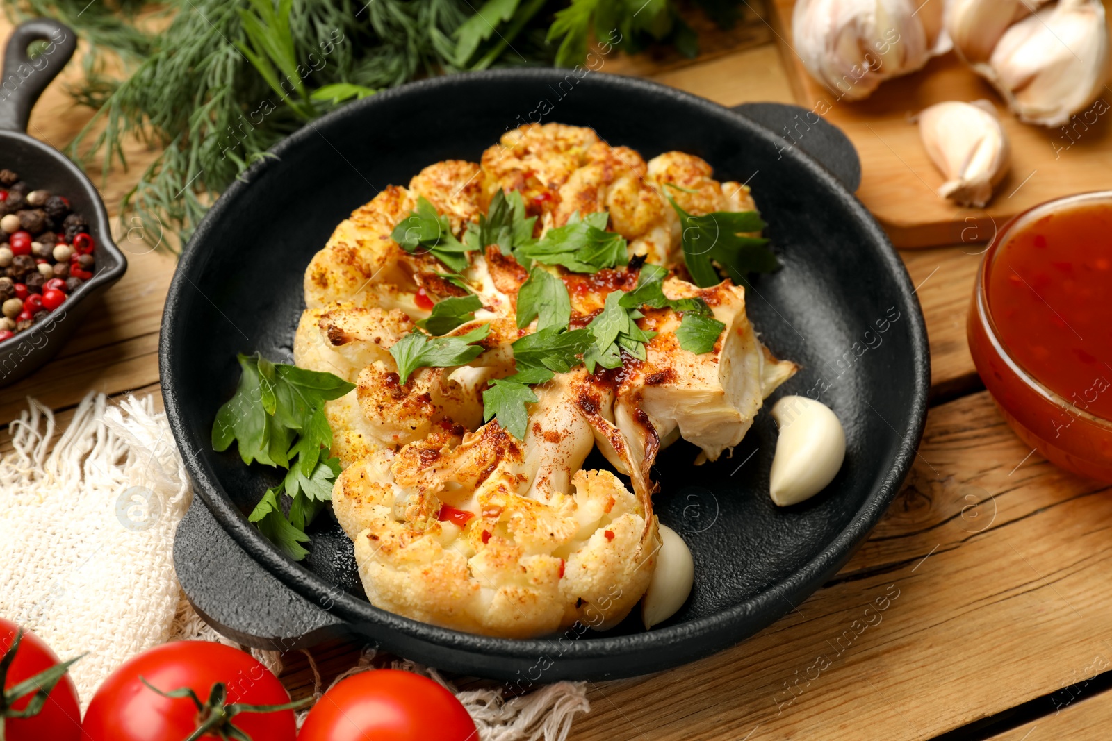 Photo of Tasty cauliflower steak in frying pan and other products on wooden table, closeup