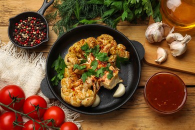 Photo of Tasty cauliflower steak in frying pan and other products on wooden table, top view