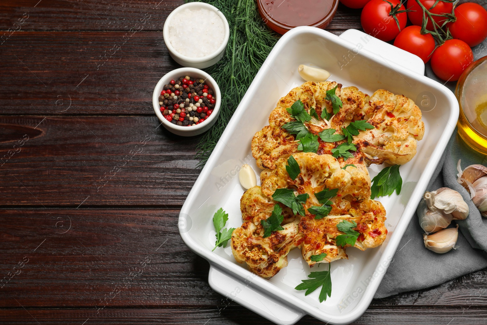 Photo of Tasty cauliflower steaks in baking dish and other products on wooden table, top view. Space for text