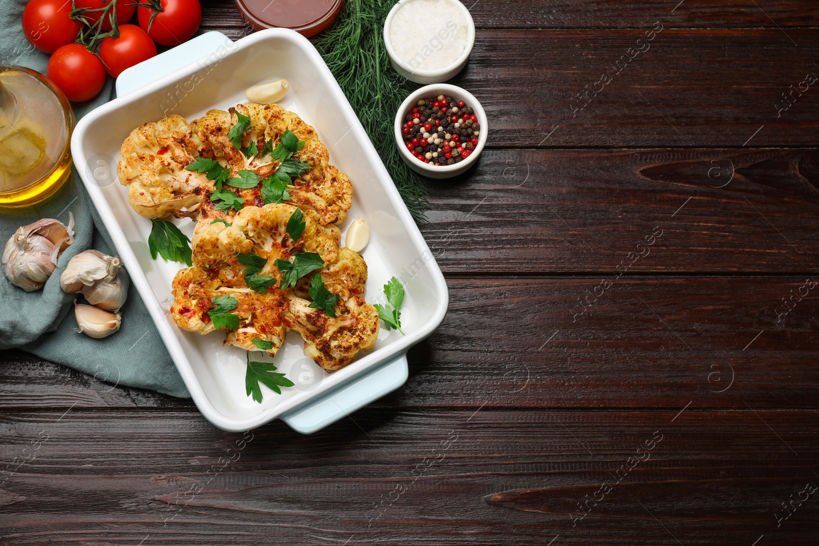 Photo of Tasty cauliflower steaks in baking dish and other products on wooden table, top view. Space for text