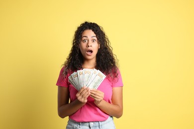 Shocked woman with dollar banknotes on yellow background