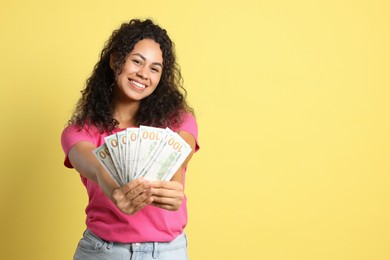 Happy woman with dollar banknotes on yellow background, space for text