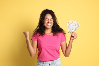 Happy woman with dollar banknotes on yellow background