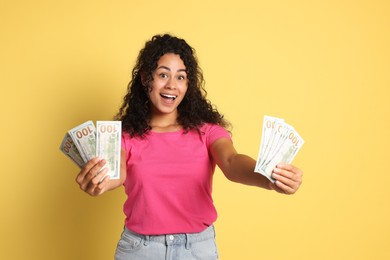 Happy woman with dollar banknotes on yellow background