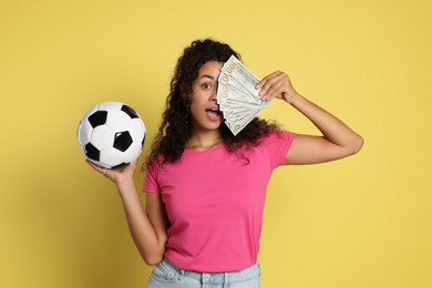 Shocked woman with money and soccer ball on yellow background