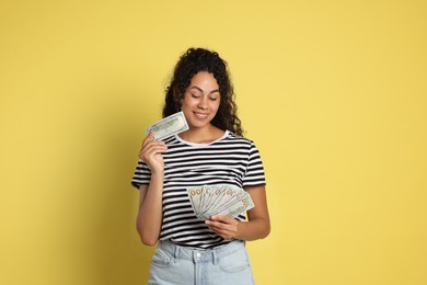 Happy woman with dollar banknotes on yellow background