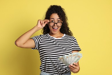 Happy woman with dollar banknotes on yellow background