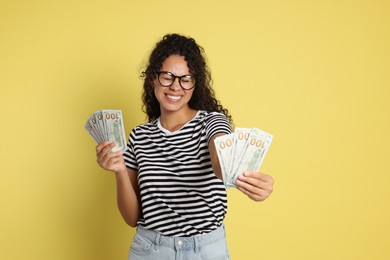 Happy woman with dollar banknotes on yellow background