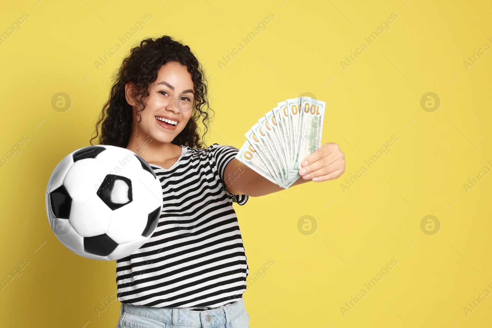 Photo of Happy woman with money and soccer ball on yellow background, space for text