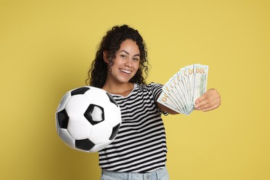 Happy woman with money and soccer ball on yellow background