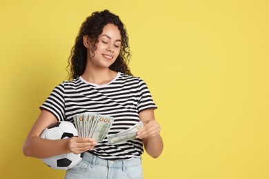 Happy woman with money and soccer ball on yellow background, space for text