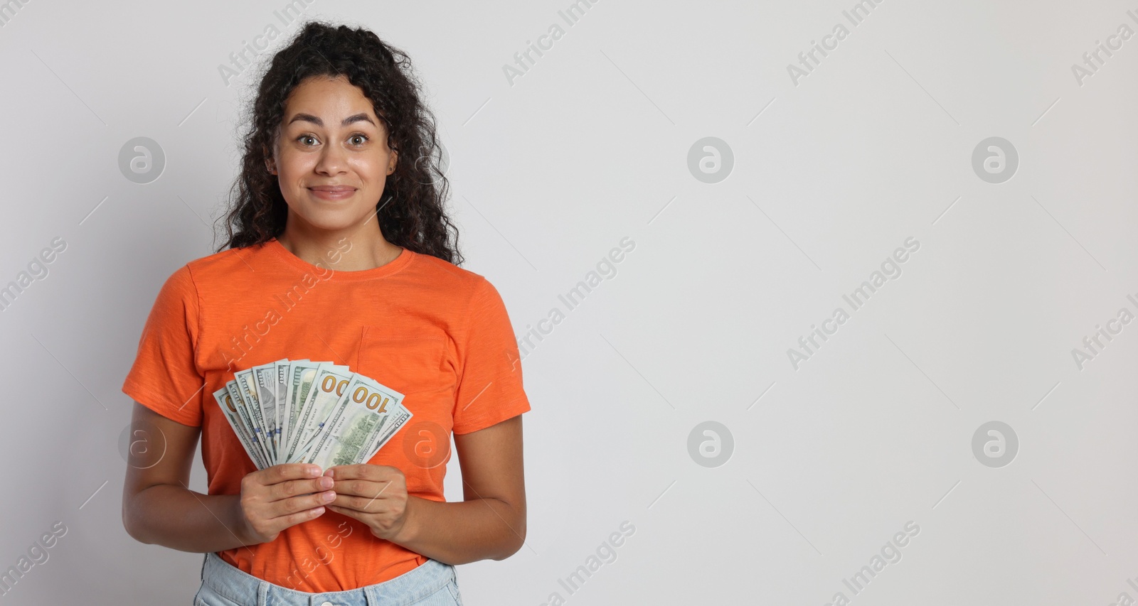 Photo of Smiling woman with dollar banknotes on light grey background, space for text