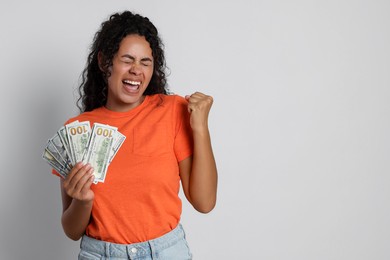 Happy woman with dollar banknotes on light grey background, space for text