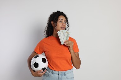 Woman with money and soccer ball on light grey background