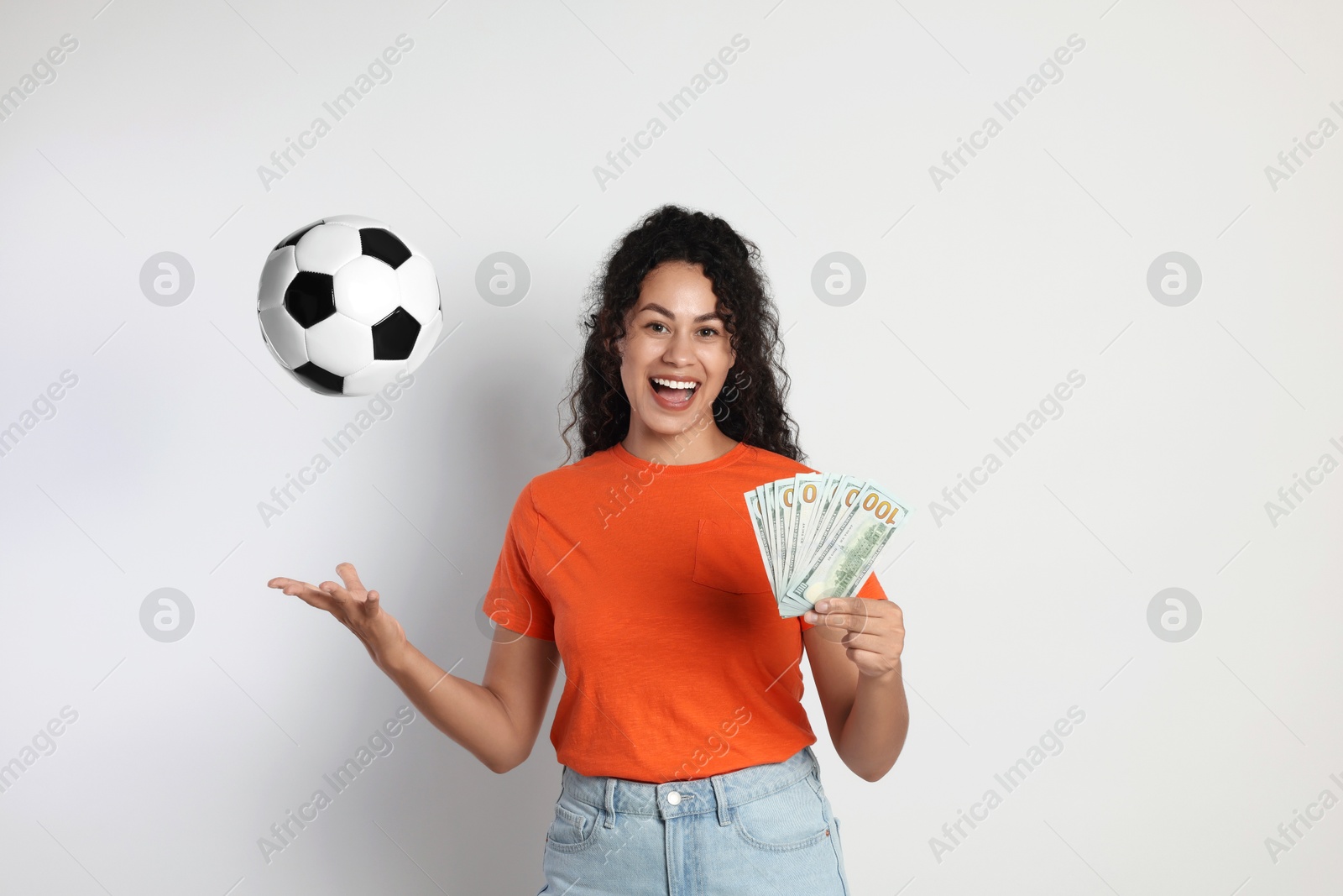 Photo of Happy woman with money throwing soccer ball on light grey background