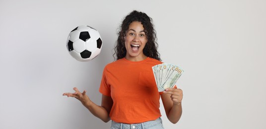 Happy woman with money throwing soccer ball on light grey background