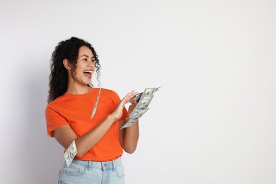 Happy woman throwing money on light grey background, space for text