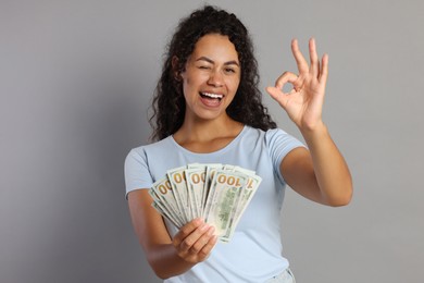 Happy woman with dollar banknotes showing ok gesture on grey background