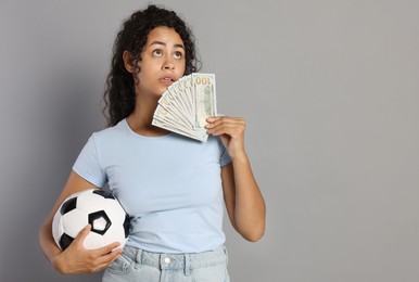 Woman with money and soccer ball on grey background, space for text