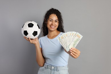 Happy woman with money and soccer ball on grey background