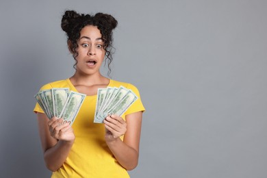 Shocked woman with dollar banknotes on grey background, space for text