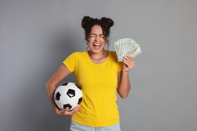 Happy woman with money and soccer ball on grey background