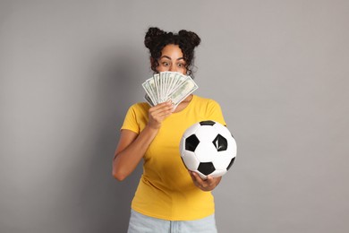 Woman with money and soccer ball on grey background