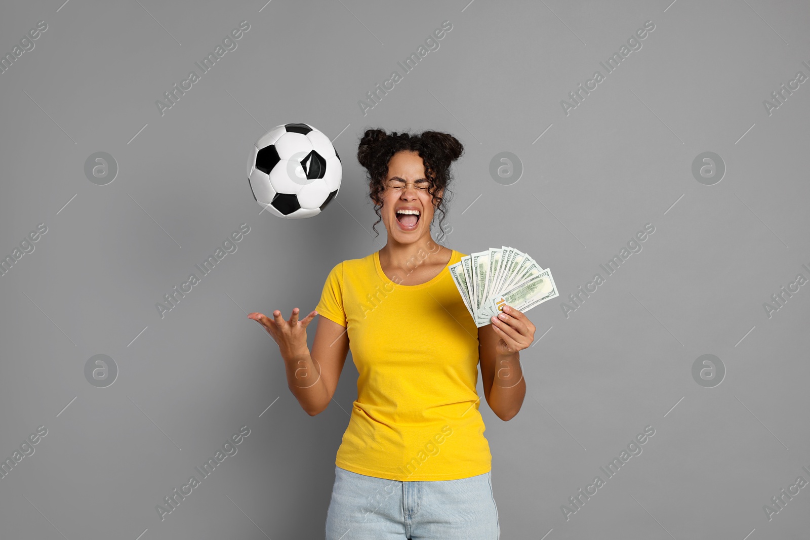 Photo of Happy woman with money throwing soccer ball on grey background