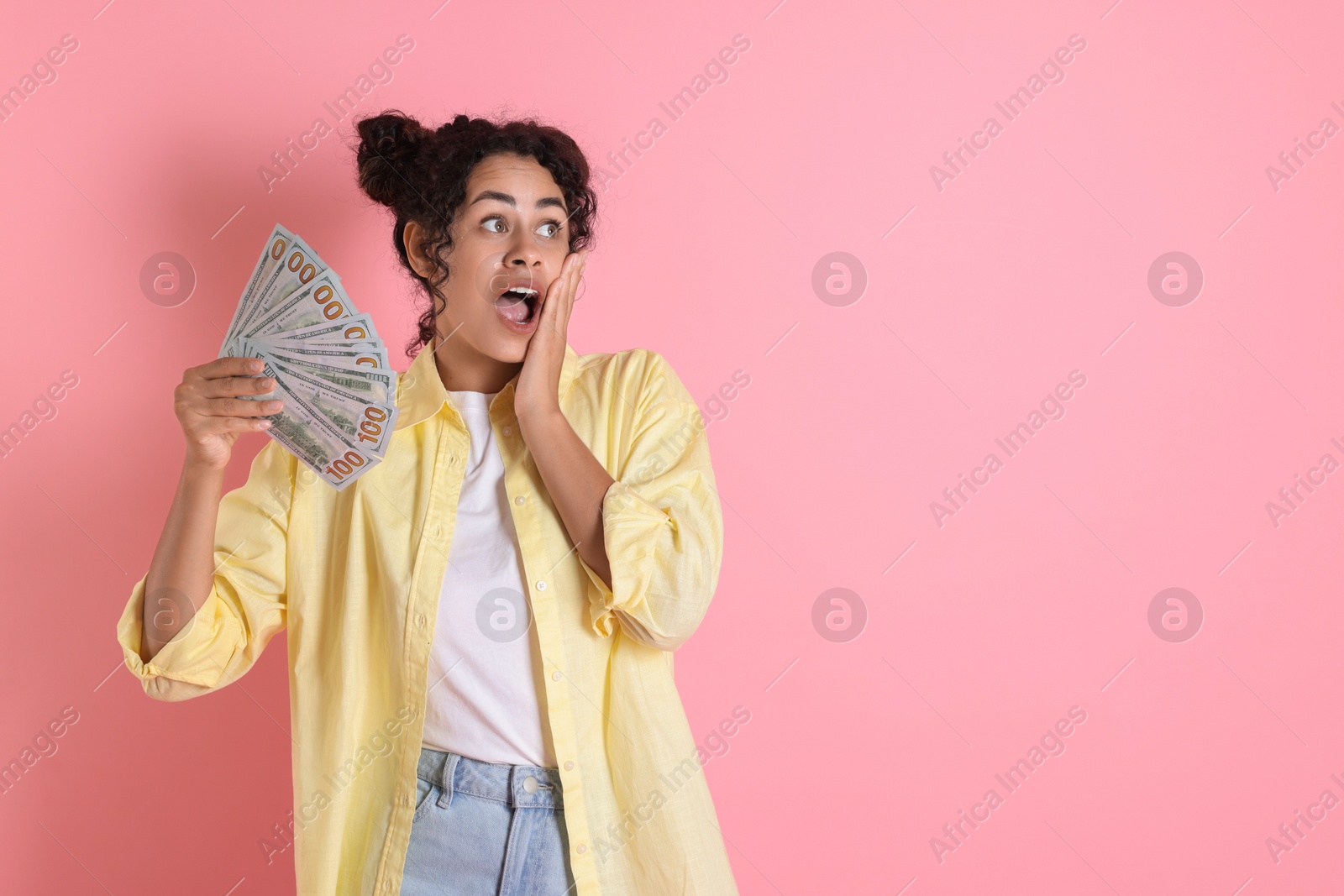 Photo of Shocked woman with dollar banknotes on pink background, space for text