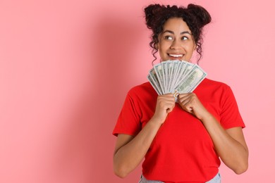 Happy woman with dollar banknotes on pink background, space for text