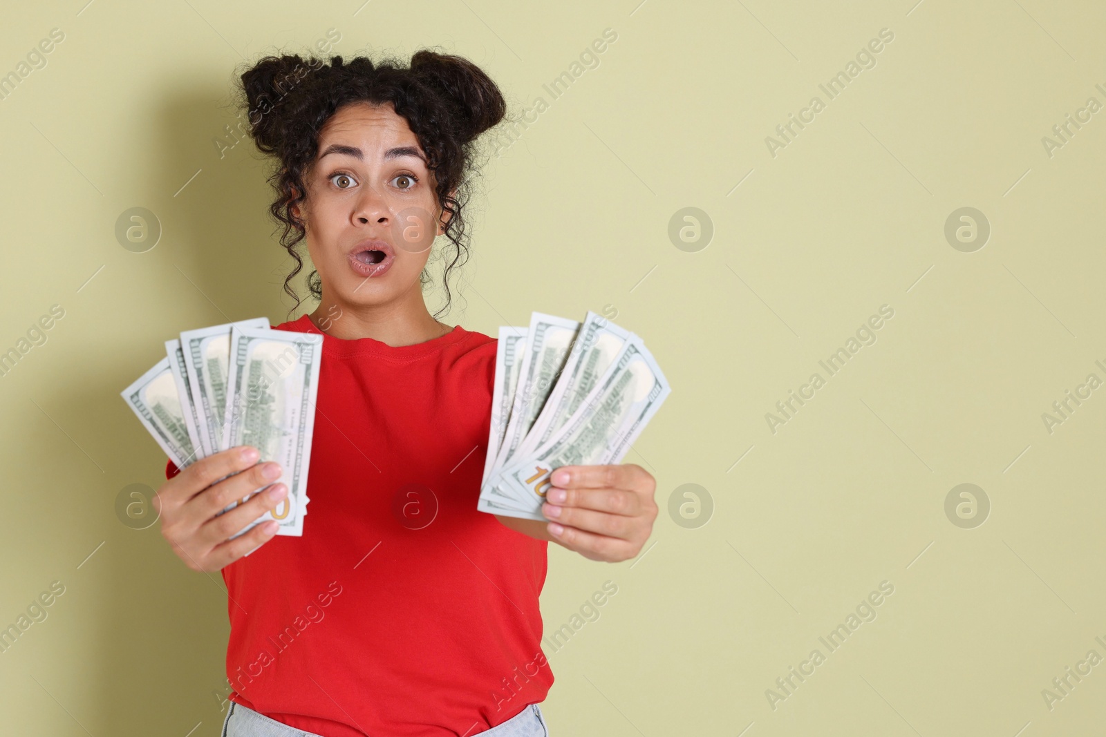 Photo of Shocked woman with dollar banknotes on pale green background, space for text